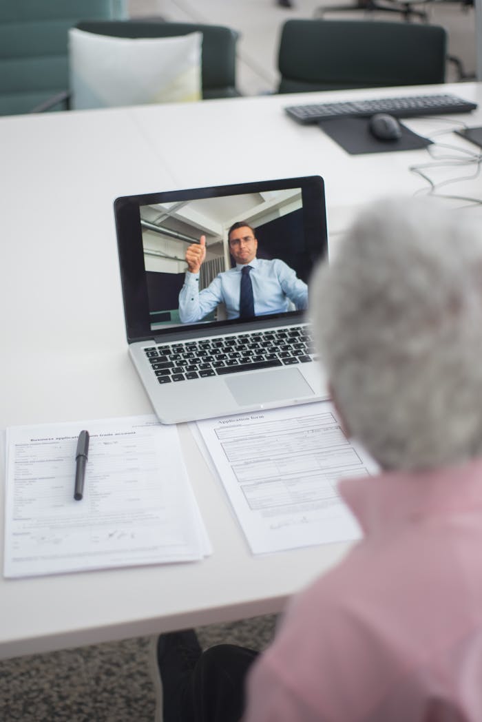 our-story Senior man engages in a video conference with a colleague on a laptop, discussing documents.